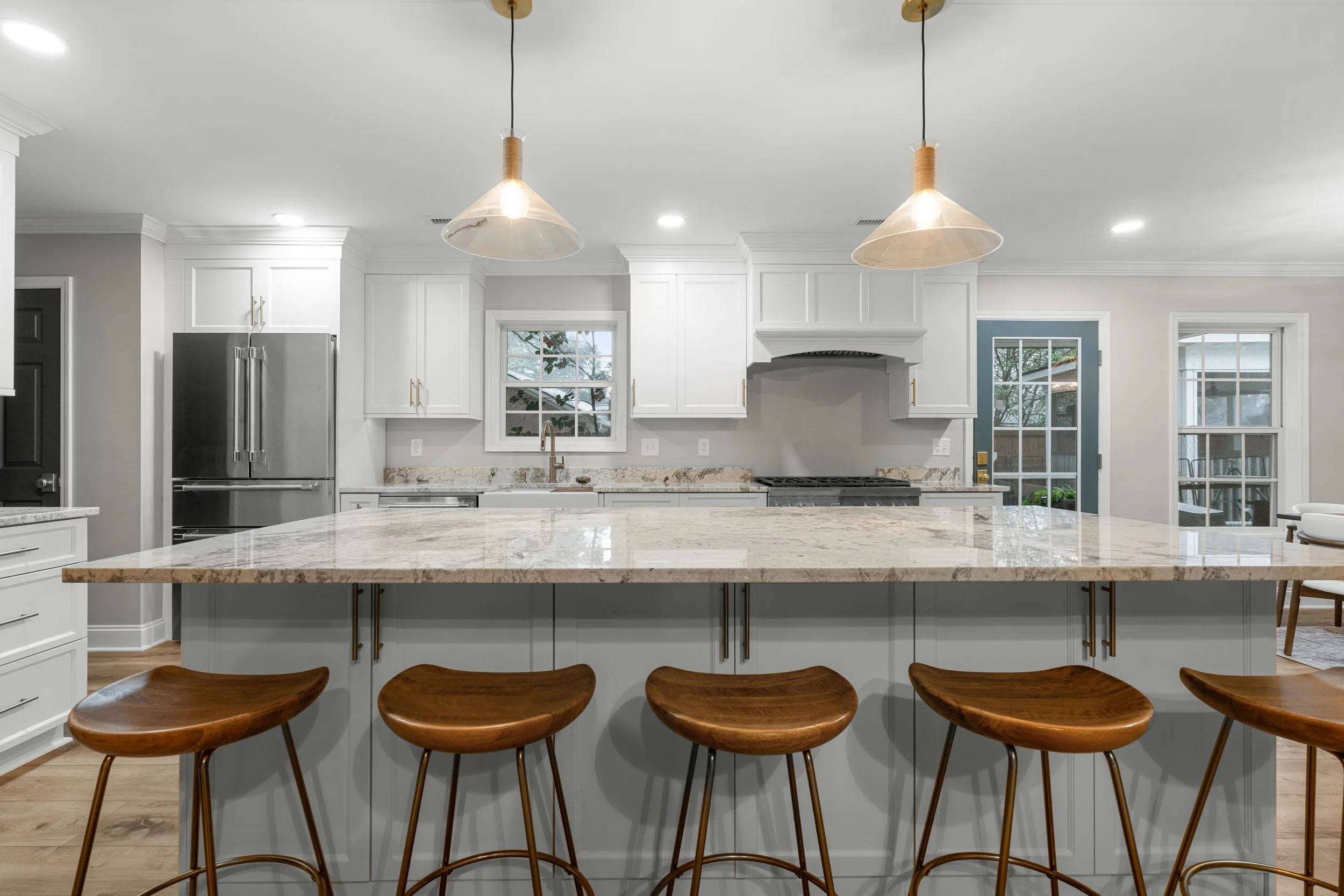 Modern kitchen with white cabinets, granite countertops, stainless steel appliances, wooden bar stools, and pendant lighting.
