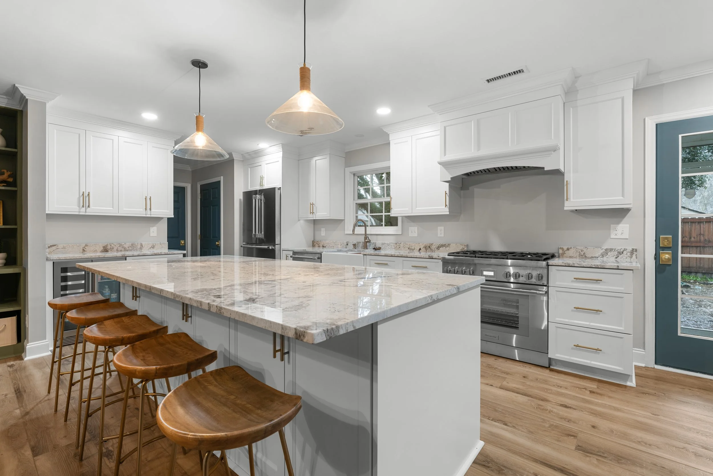 Modern kitchen with a large marble island, white cabinets, stainless steel appliances, and hardwood floors.