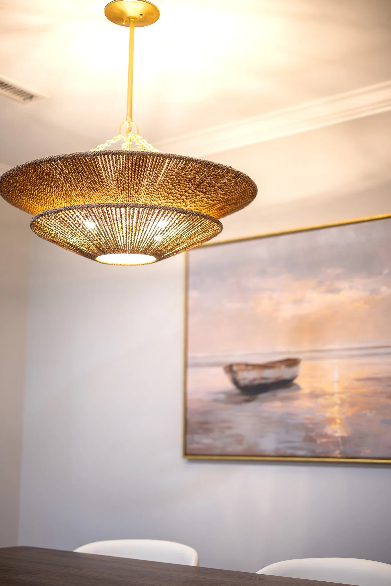 Interior of a room with a golden hanging light fixture and a framed landscape painting on the wall.