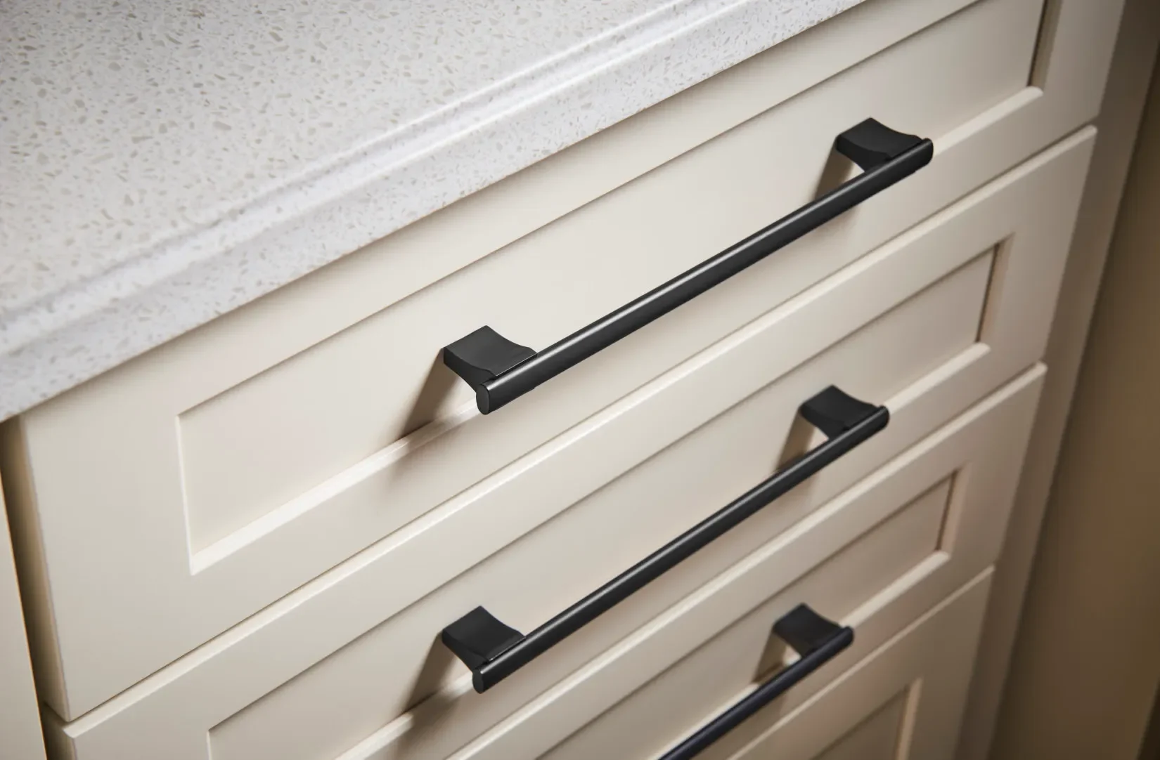 Close-up of cream-colored kitchen cabinet drawers with black handles.