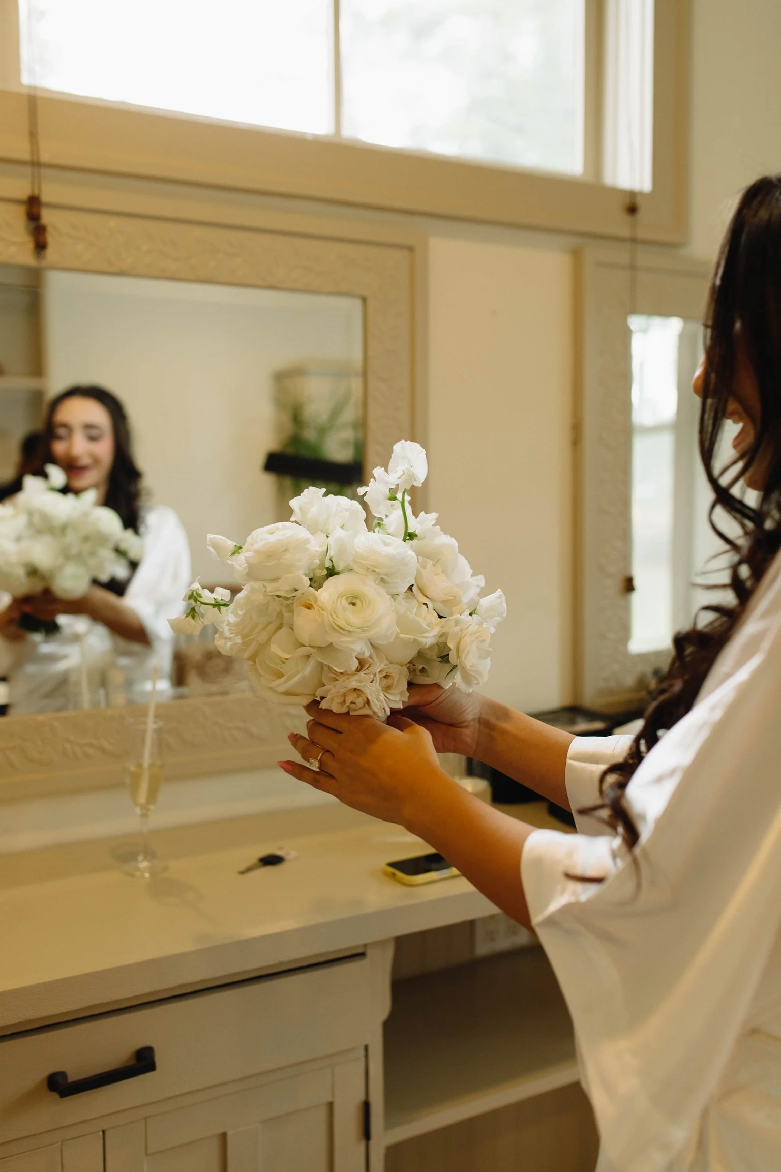 The bride holds her delicate bouquet of white roses, ranunculus, majolica roses, and sweet peas. She is wearing a square cushion cut diamond on her finger.