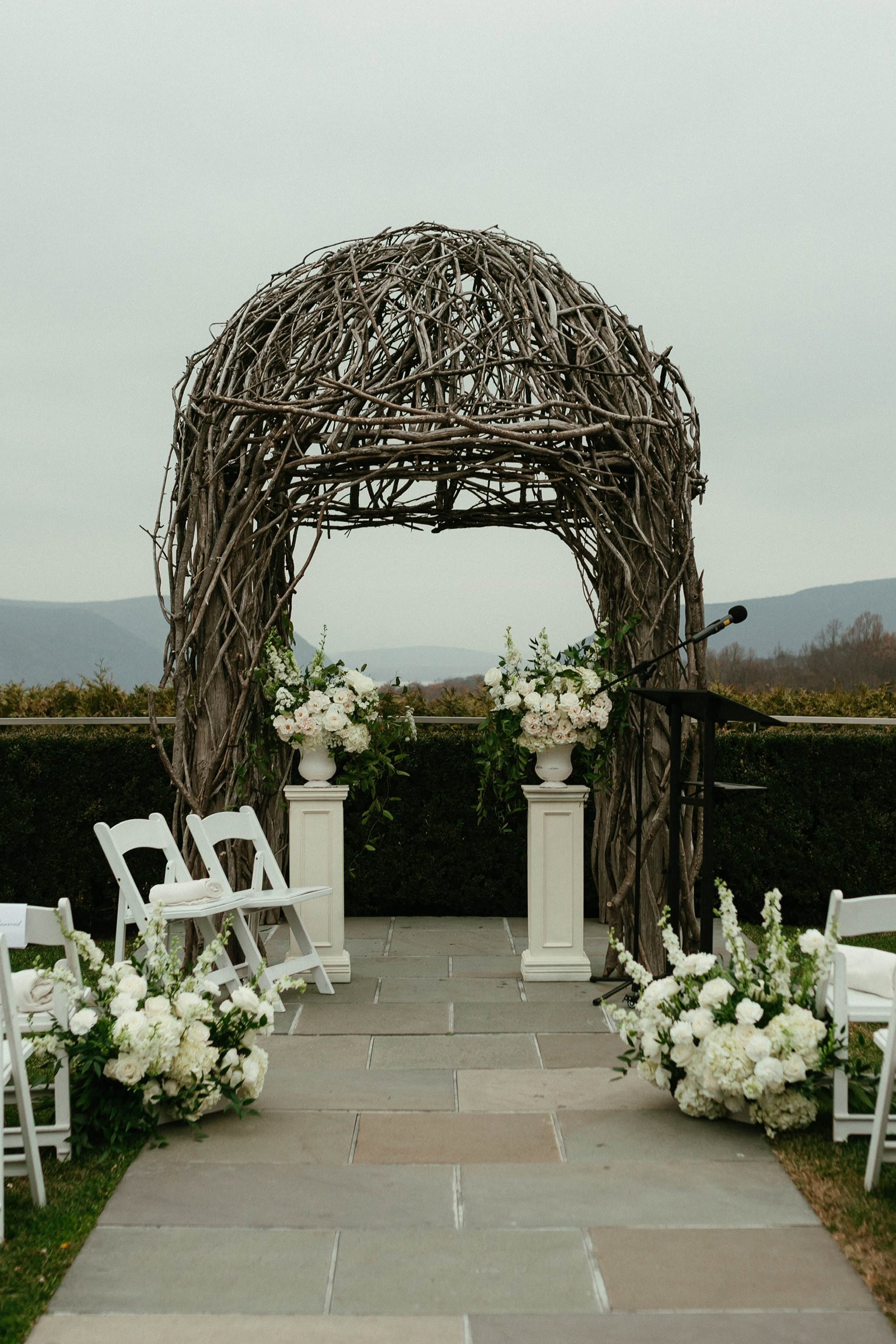 The Garrison pergola with 2 white floral arrangements on pedestals and 2 white floral ground pieces on the inside of the end of the aisle