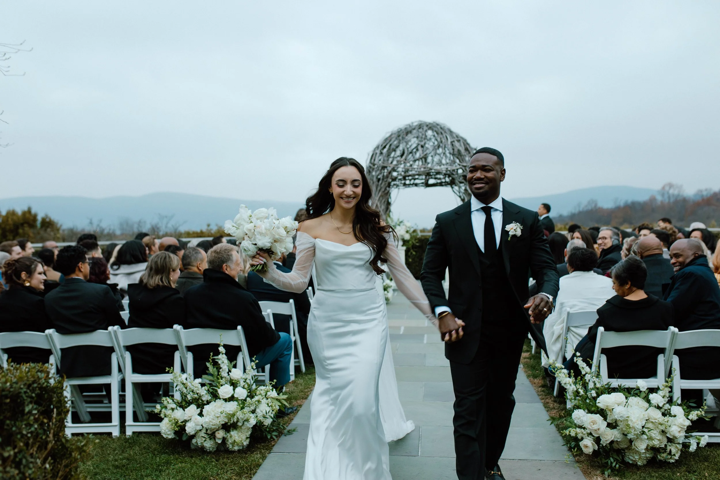 Happy couple walking down the aisle after getting married. The bride looks elated and s holding her white bridal bouquet in her right hand, while holding her new husband's hand with her left hand