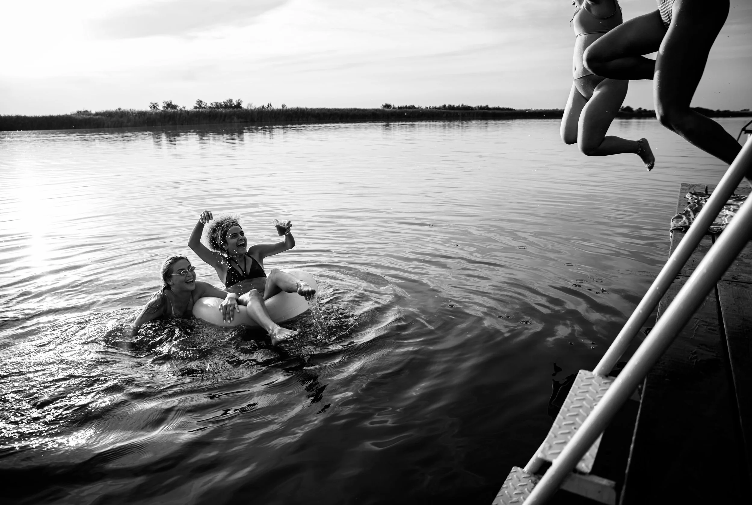 Tres niñas divirtiéndose en el agua, una en una cámara inflable con otra niña y una tercera saltando desde una barda hacia el agua en un entorno natural.