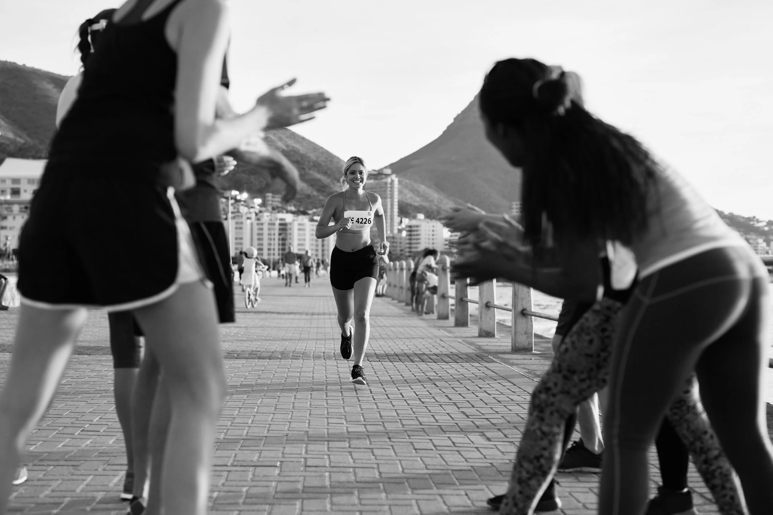 Mujer corriendo en una carrera junto a la playa con espectadores animándola.