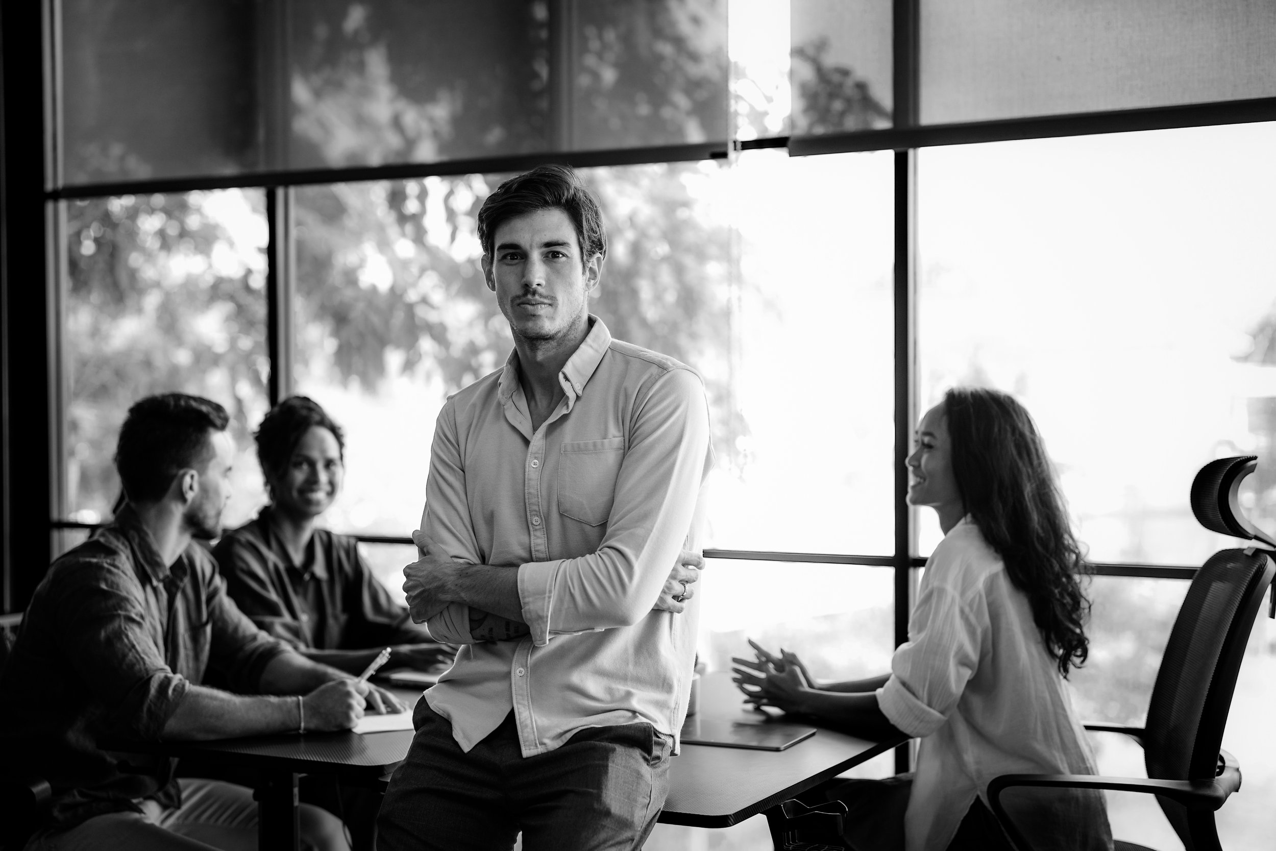 Un grupo de cuatro personas en una sala de reuniones, con un hombre en primer plano que mira hacia la cámara, y tres personas en el fondo conversando y sonriendo.