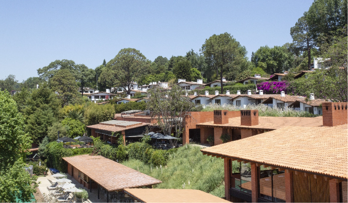 Residential hillside with multiple houses, trees, and lush greenery under a clear blue sky.