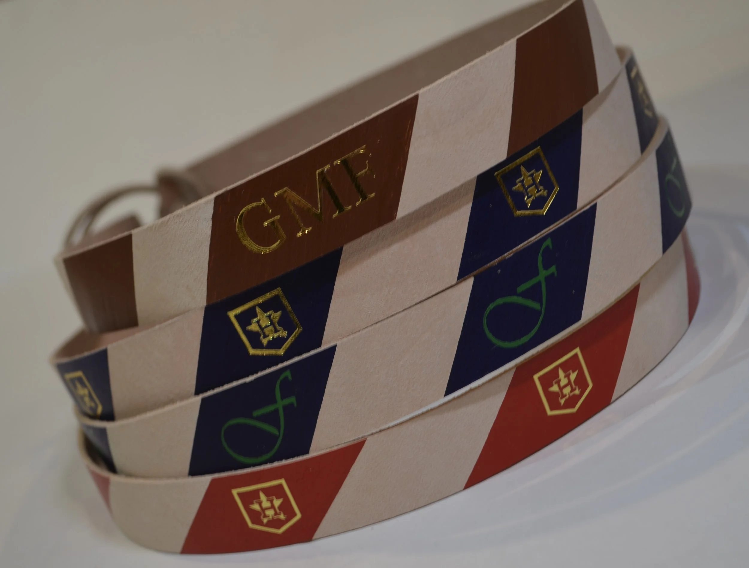 Three barber paper strips with red, white, and blue diagonal stripes, featuring a logo with a shield and a hairstyle icon, and the phrase 'Groom' in gold, set against a neutral background.