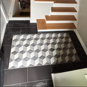 Entryway with a geometric patterned rug, black tiled floor, and wooden stairs with white risers.