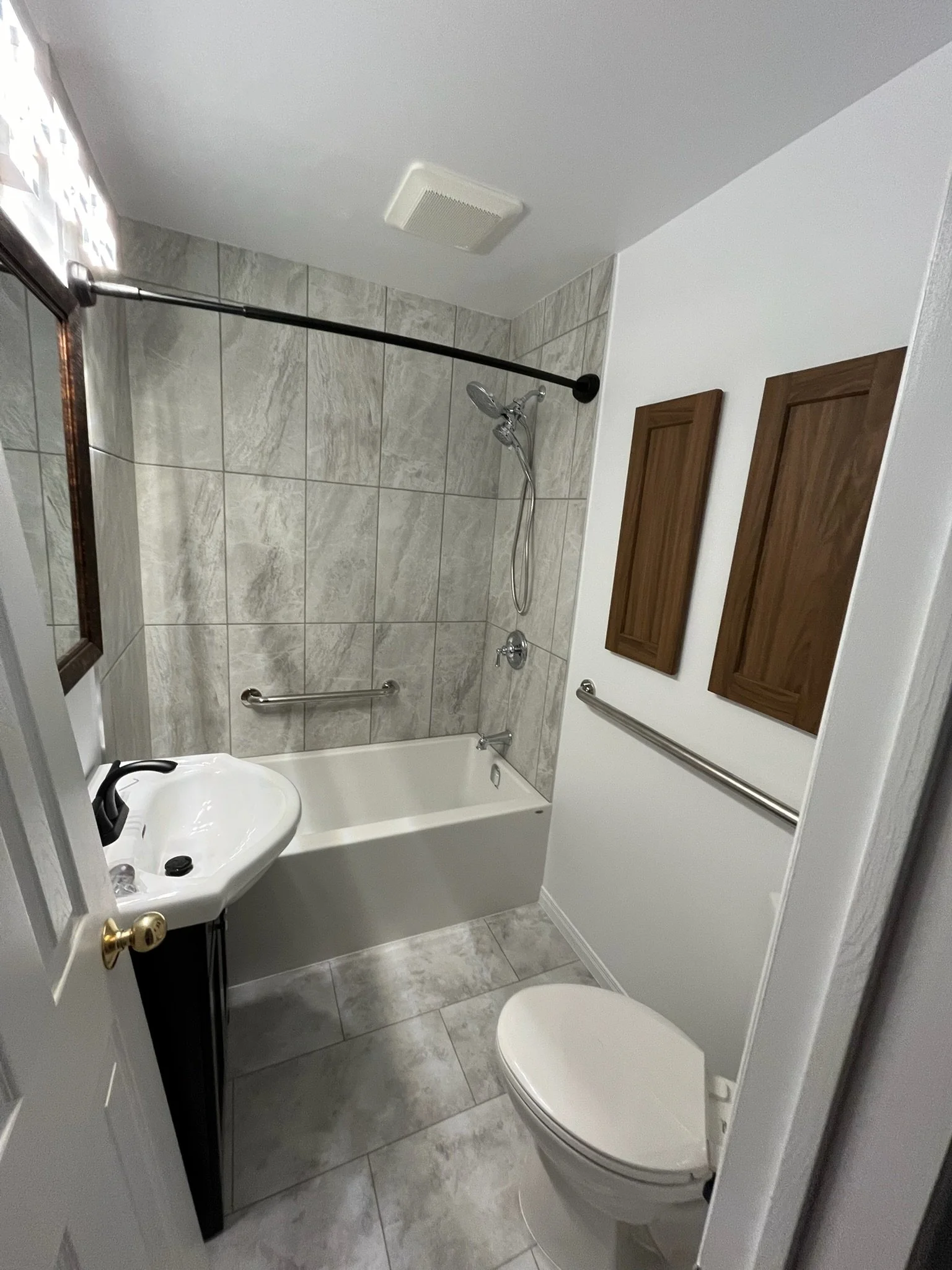 Small bathroom with a bathtub, a handheld shower, a toilet, and a small sink. The walls have wood paneling and the floor is tiled.