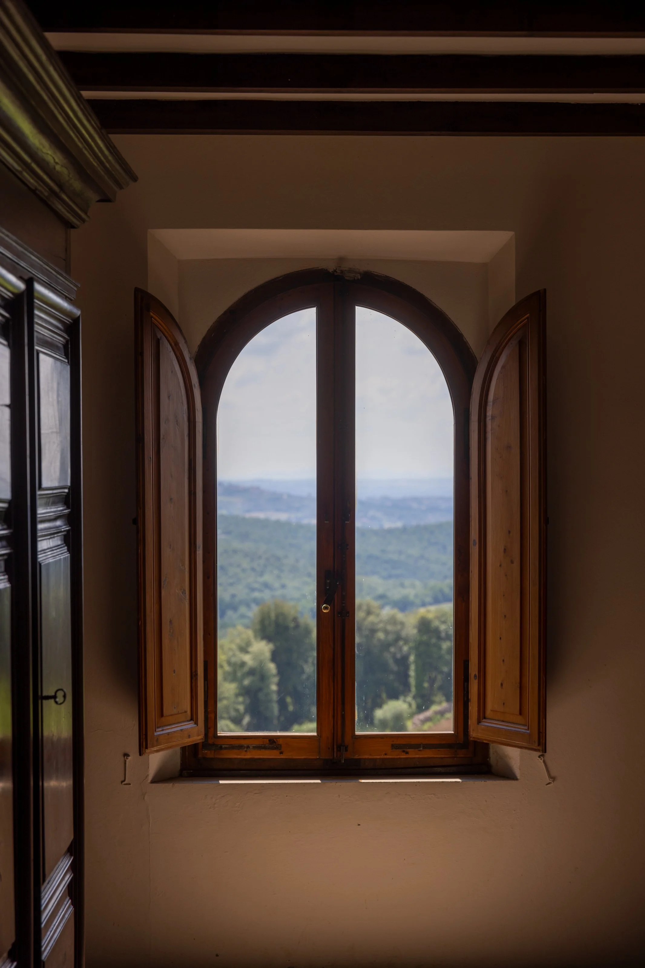 Open wooden window with a scenic view of green hills and a distant landscape.