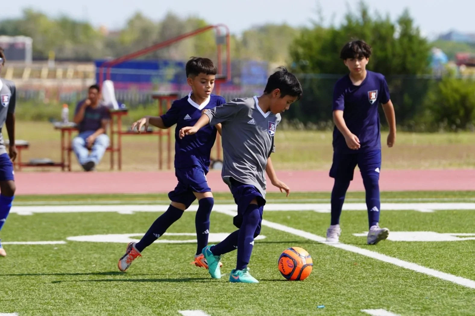 Group of children and two adults posing for a photo outdoors in front of a modern building with large windows and a tree.