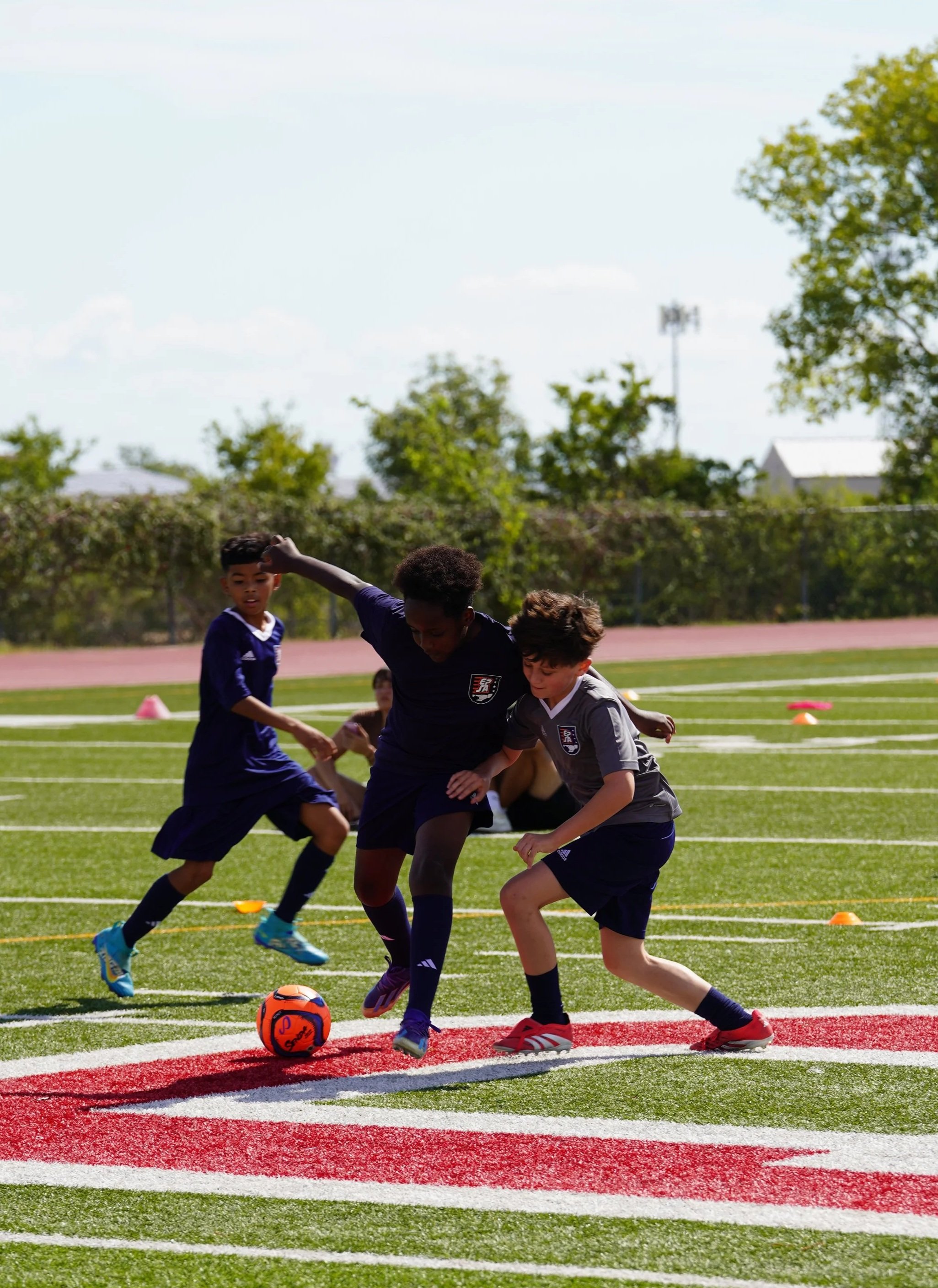Group of children and coaches posing outdoors in front of a school building on a sunny day.