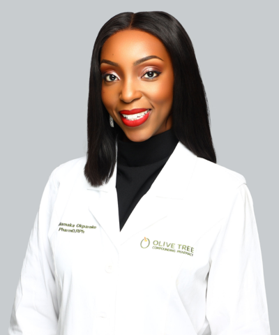 Professional woman with long straight black hair, red lipstick, wearing a white lab coat with Olive Tree Counseling Pharmacy logo, white blouse, against light gray background.