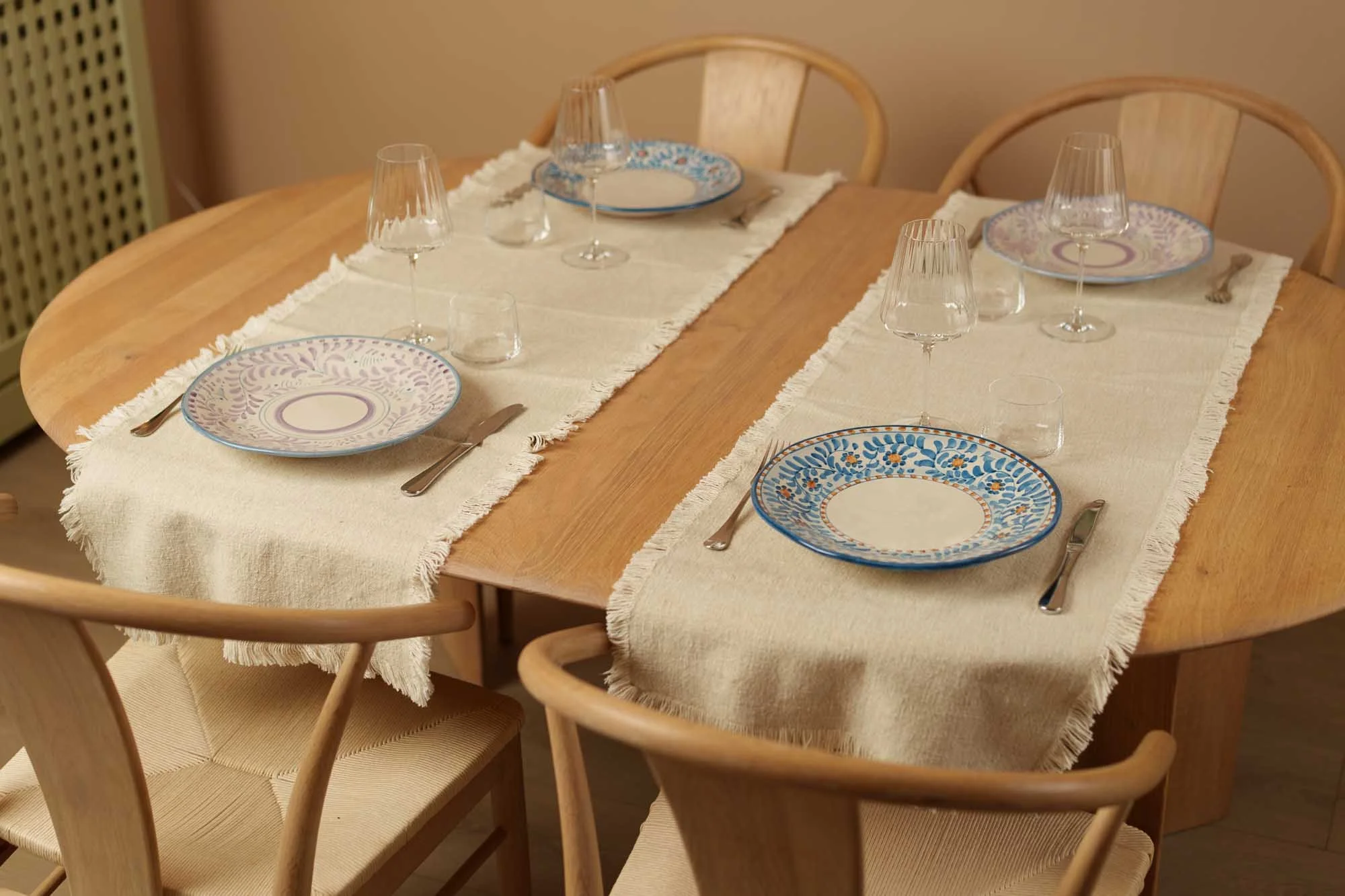 Spisebord i tre dekket med nøytrale linløpere og fargerike, håndmalte italienske keramikktallerkener.
