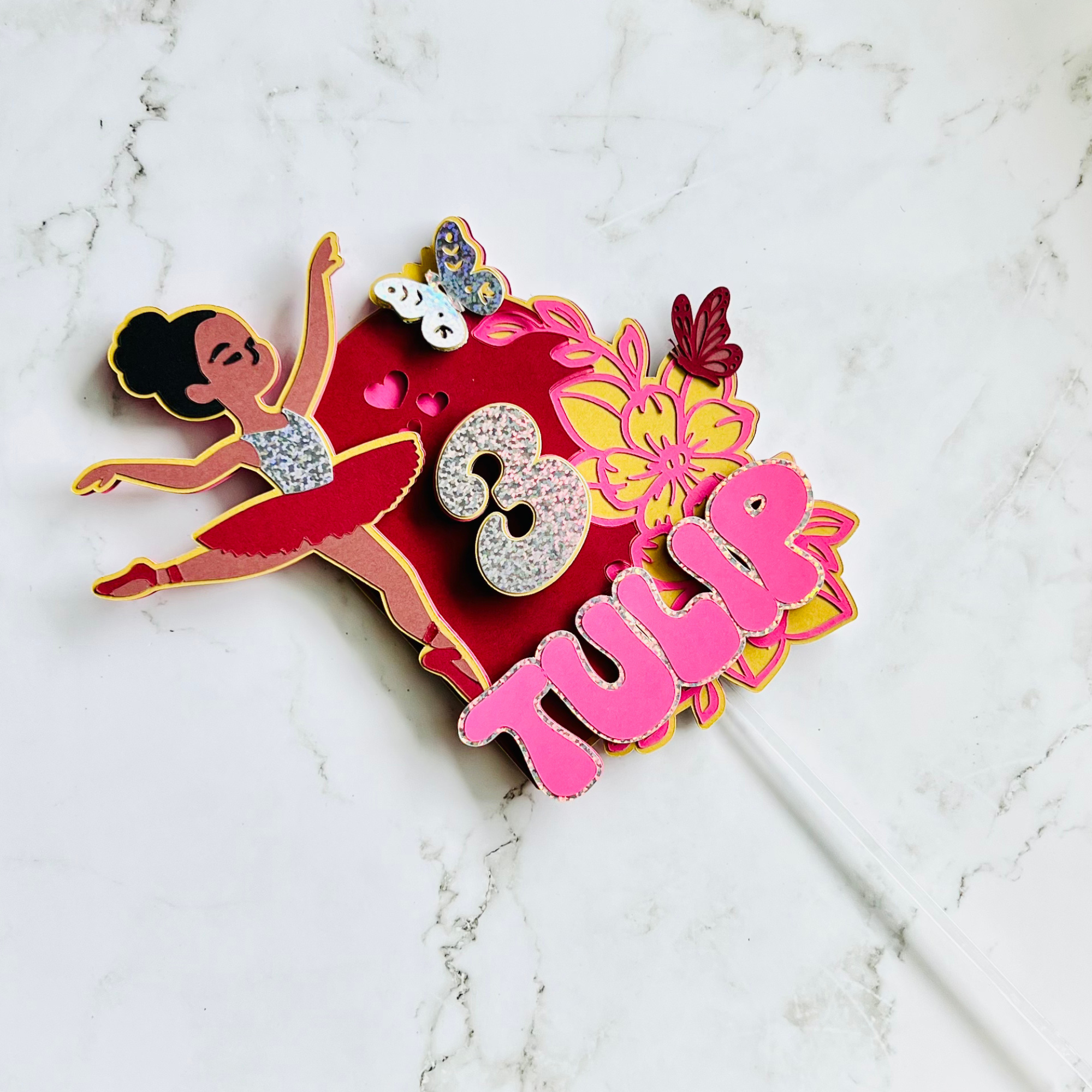 Colorful birthday cake topper with a ballerina, the number 3, flowers, butterflies, and the word 'Happy' in pink