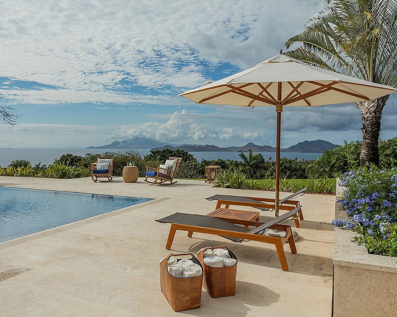 Poolside patio with lounge chairs, umbrella, and ocean view.