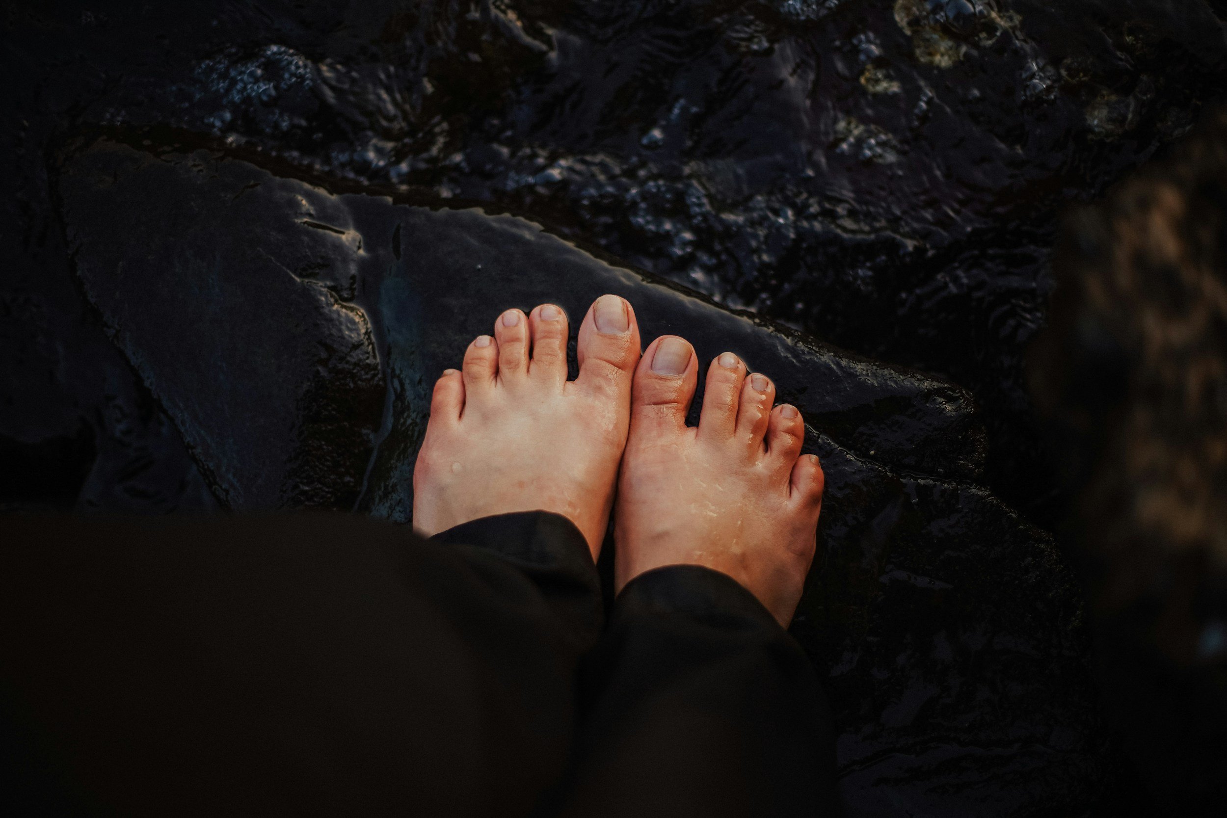 A person's bare feet standing on wet, dark rocks.