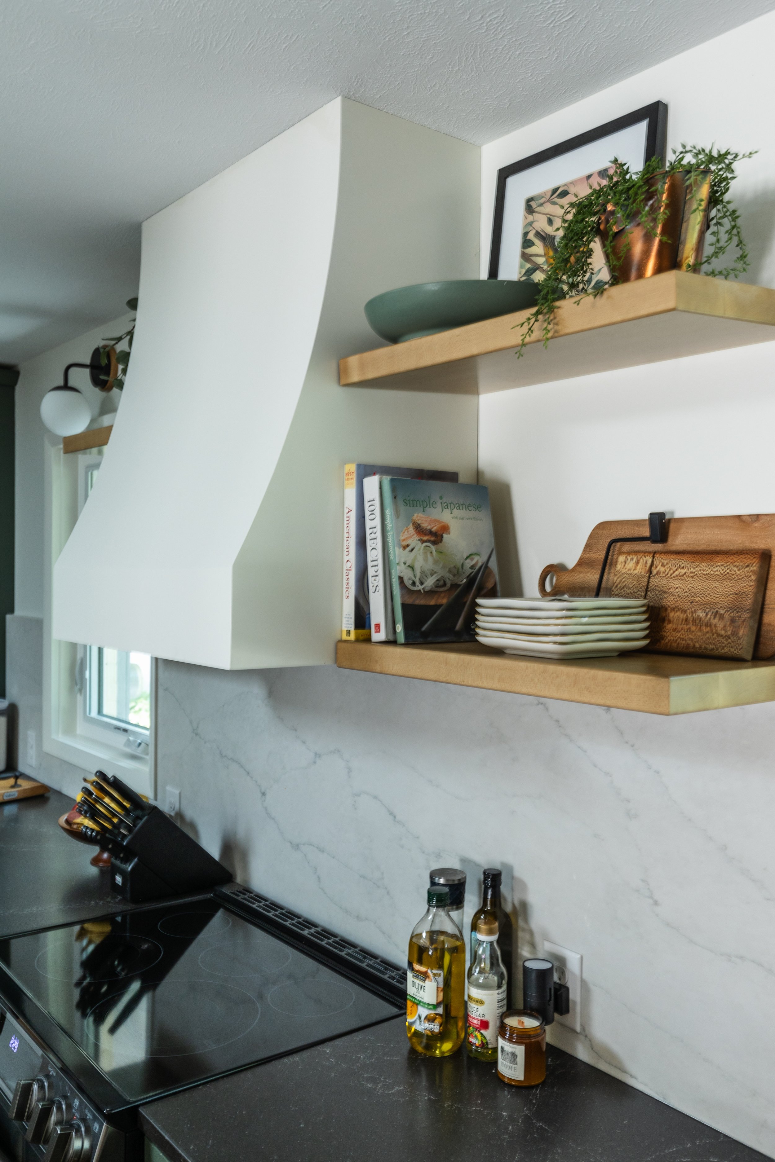 1962 Kitchen Remodel, dark green cabinets, white quartz island, wooden floors, brass hardware, wood cabinets, custom hood, floating shelves, dark countertops, open shelving, large windows.