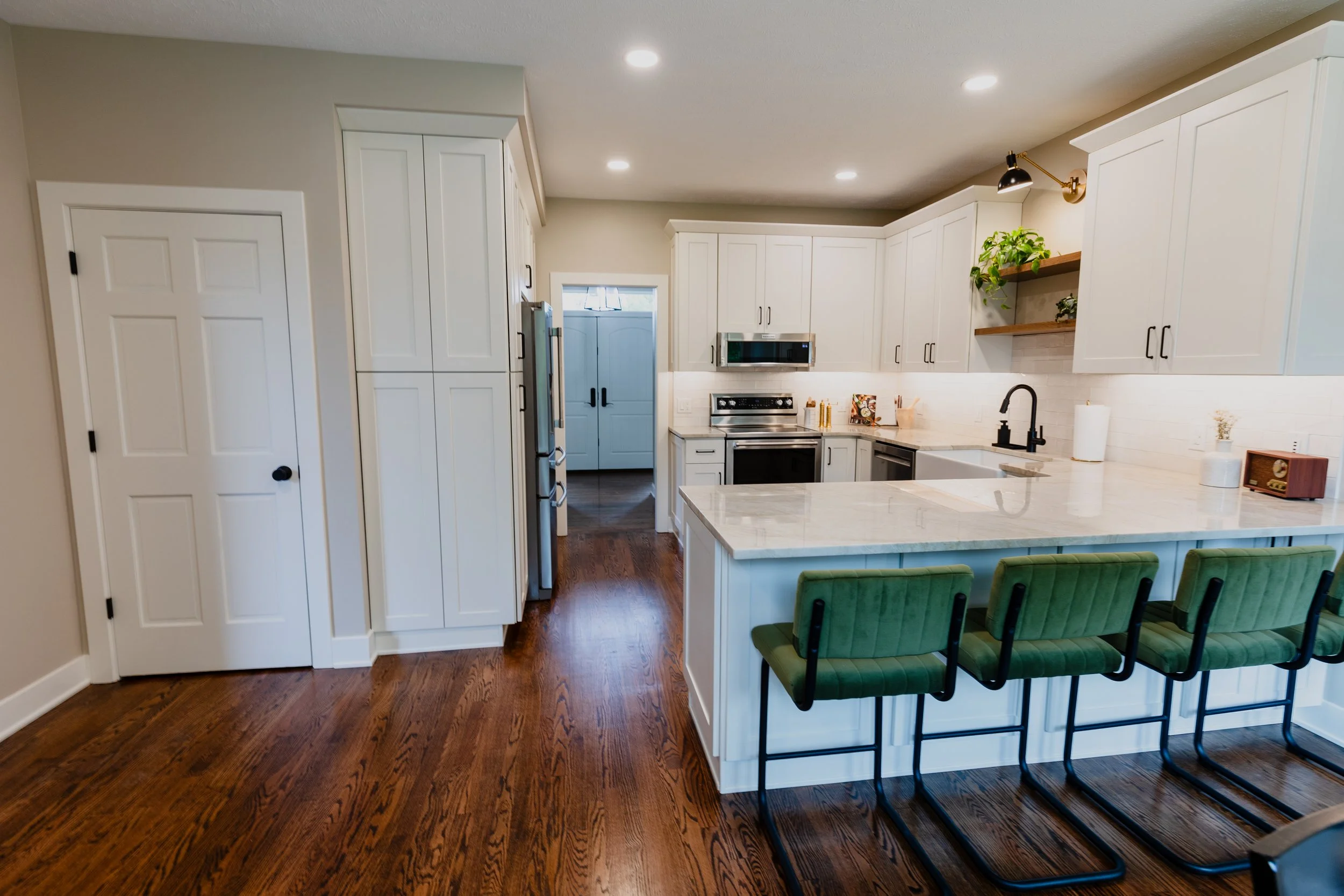 Modern kitchen with white cabinets, marble countertop island, green bar stools, hardwood floors, and stainless steel appliances.