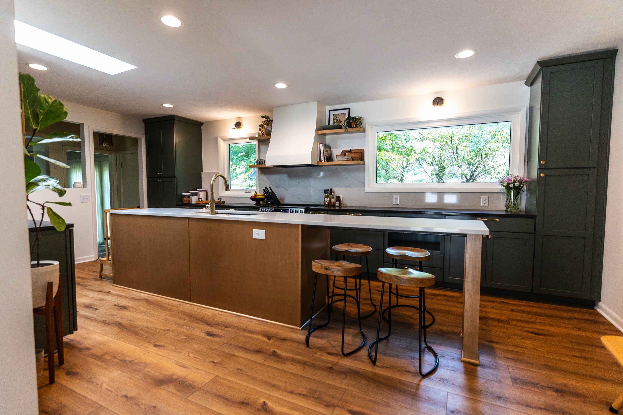 1962 Kitchen Remodel, dark green cabinets, white quartz island, wooden floors, brass hardware, wood cabinets, custom hood, floating shelves, dark countertops.