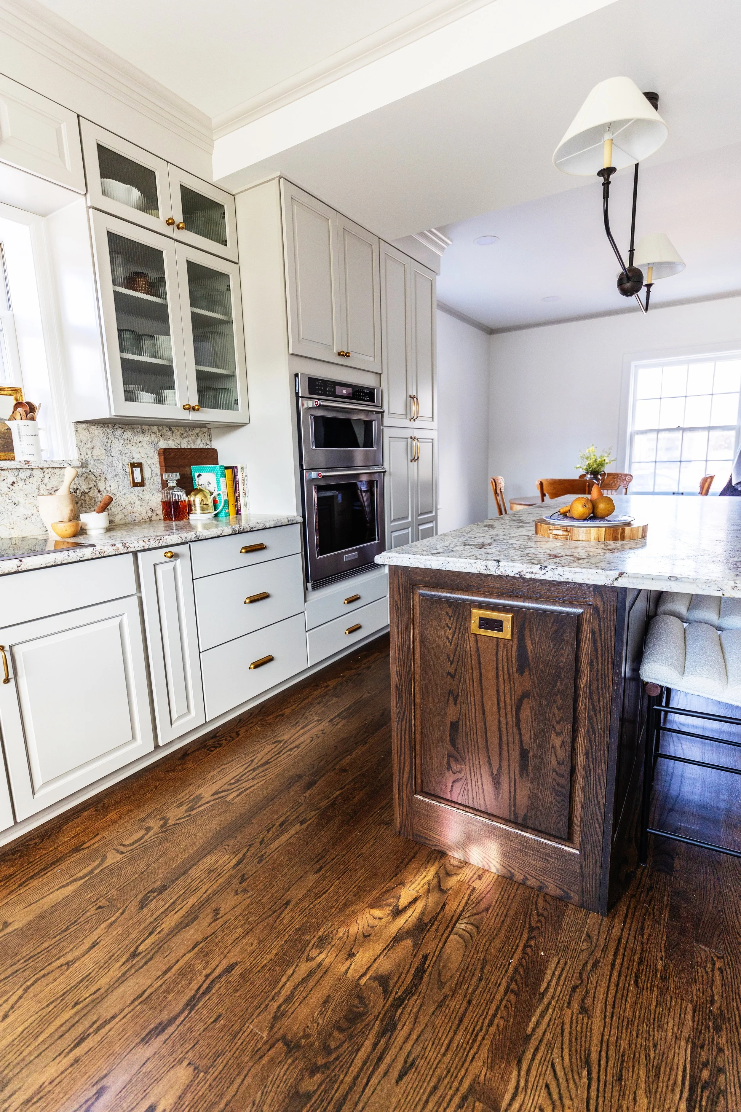 Kitchen with white cabinets, granite countertops, a wooden island, a double wall oven, and a dining area with a window and chandelier.
