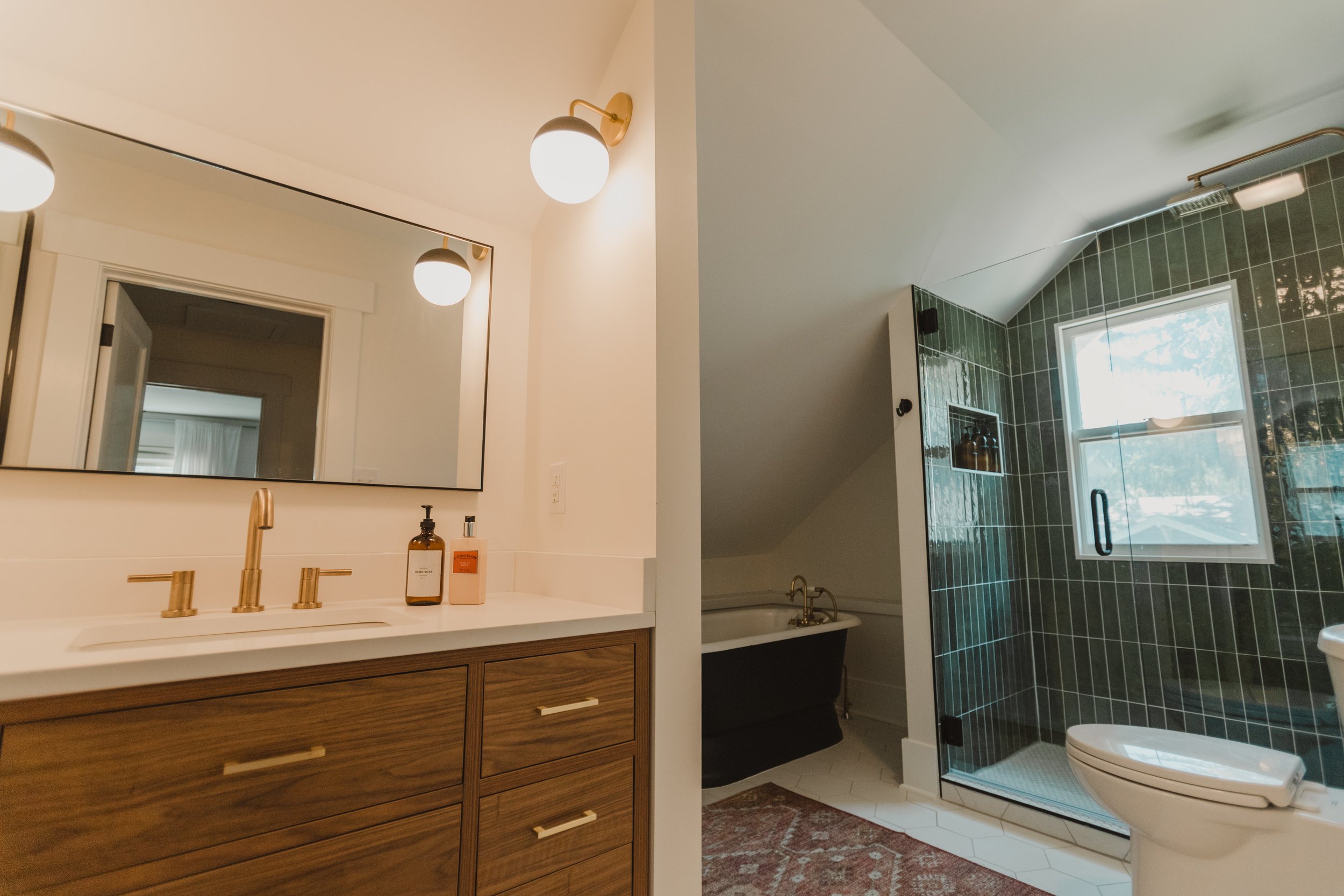 1920 Bathroom Remodel, custom wood vanity, brushed gold faucet, brushed gold sconces, modern design, mixed metal finishes, bathtub, green subway tile, white hexagon floor tile, Lincoln Nebraska, professional contractors, remodeling and renovations.