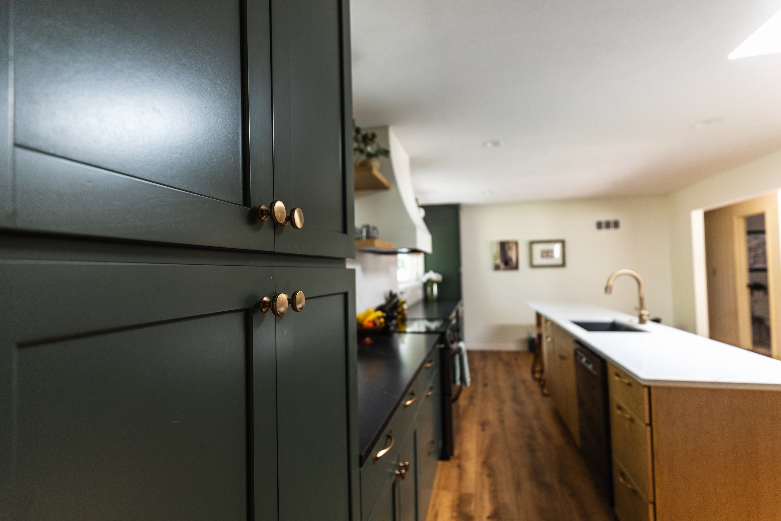 1962 Kitchen Remodel, dark green cabinets, white quartz island, wooden floors, brass hardware, wood cabinets, custom hood, floating shelves, dark countertops, open shelving, large windows, craftsmanship, custom cabinets.