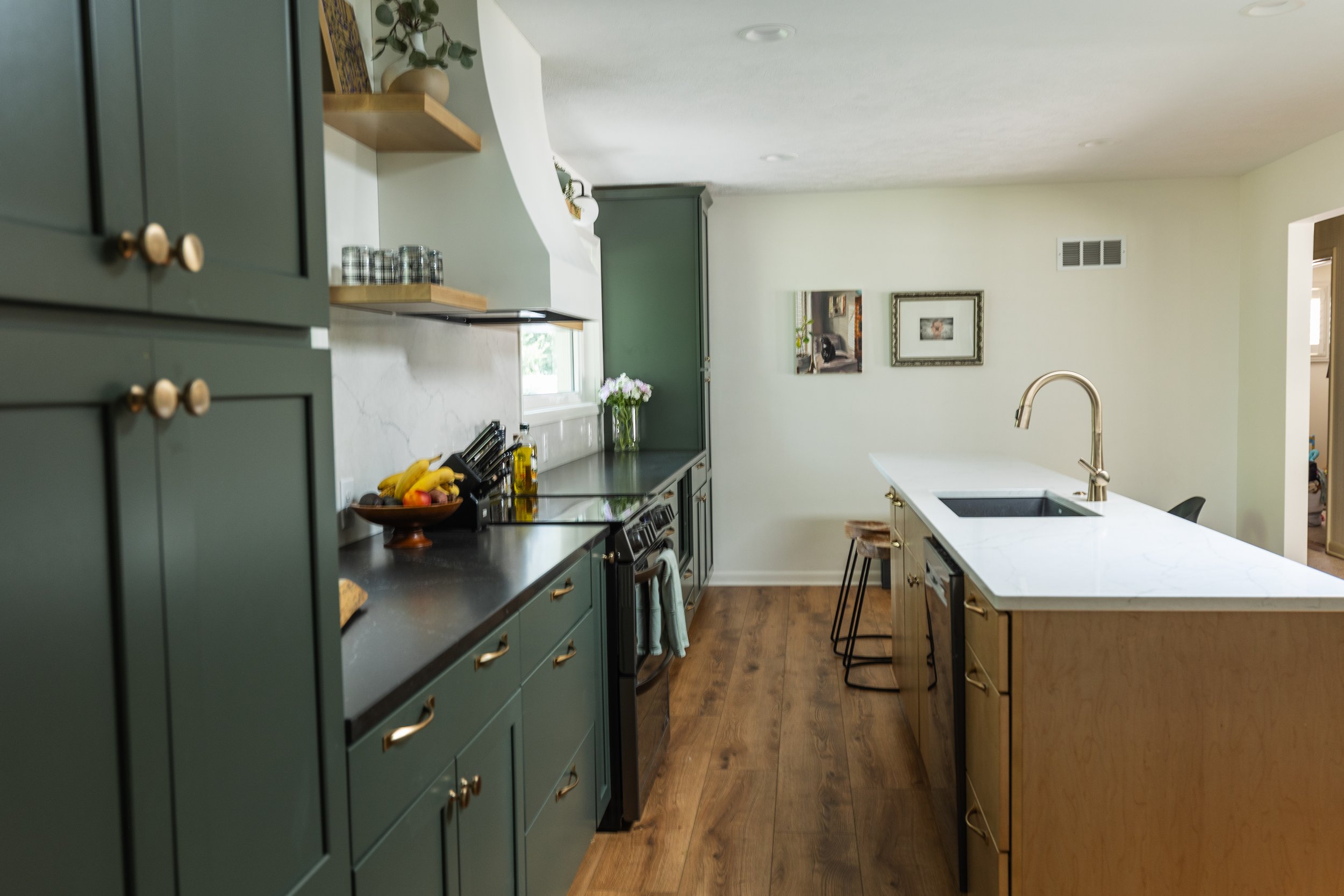 1962 Kitchen Remodel, dark green cabinets, white quartz island, wooden floors, brass hardware, wood cabinets, custom hood, floating shelves, dark countertops.