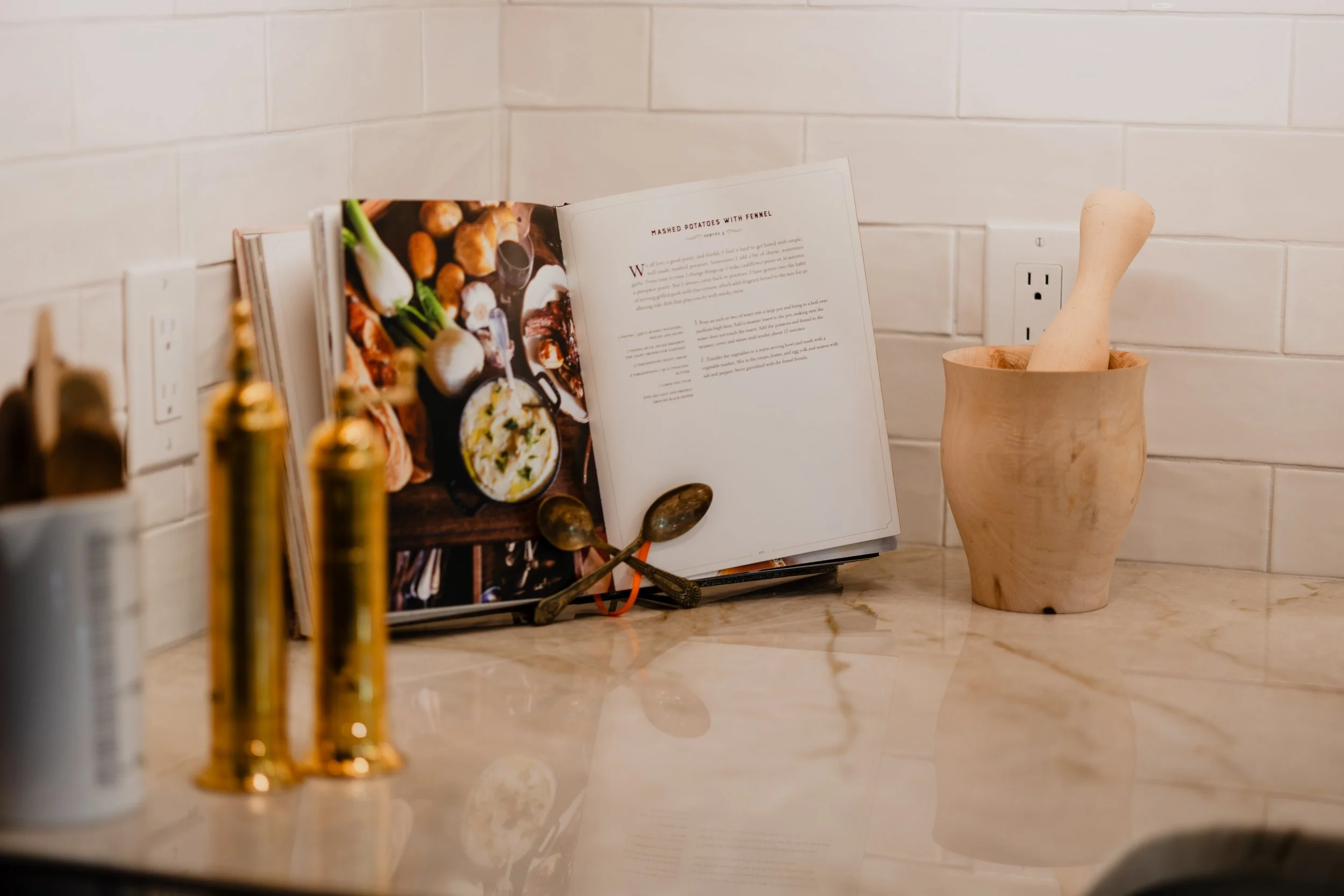Open cookbook and mortar with pestle on kitchen counter with spice bottles. 1935 Kitchen Remodel. White Subway Backsplash. Quartz Countertop.