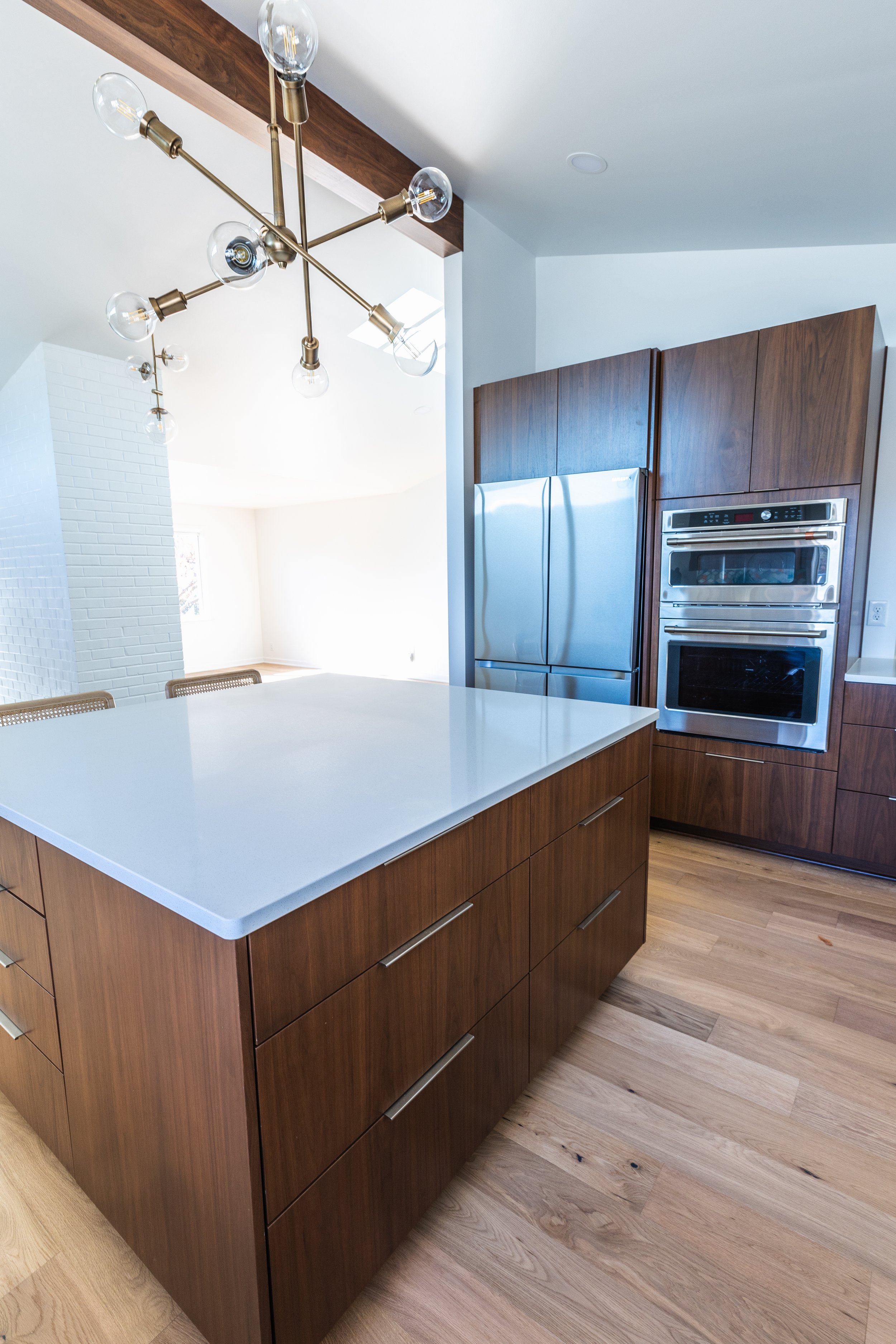 Modern kitchen with a large white island, wooden cabinets, stainless steel appliances, and a contemporary brass chandelier.