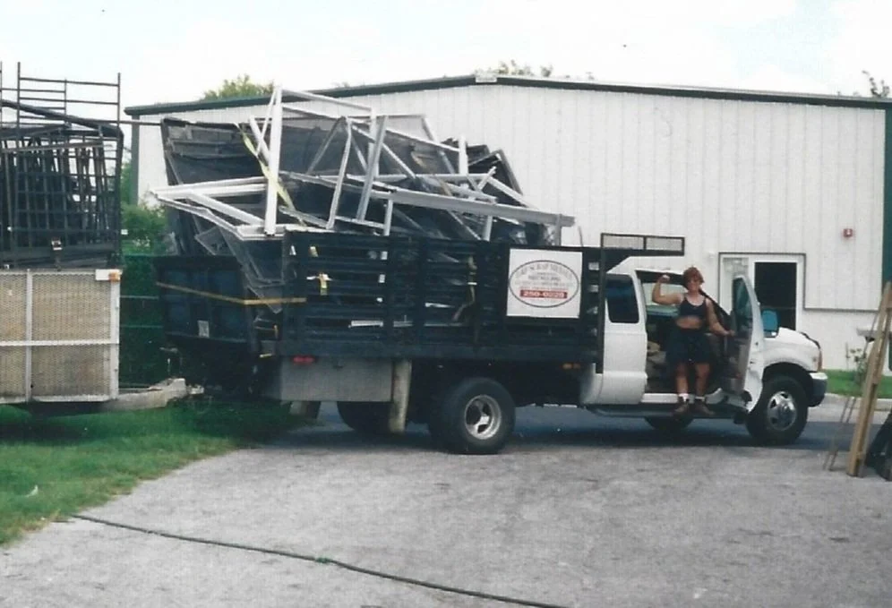 Women standing in scrap truck with metal in the background
