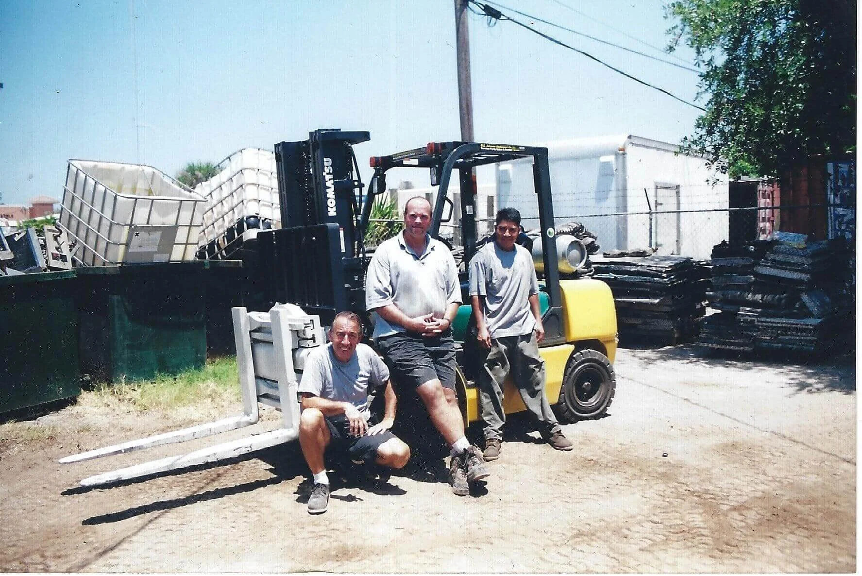 three men group photo in front of forklift