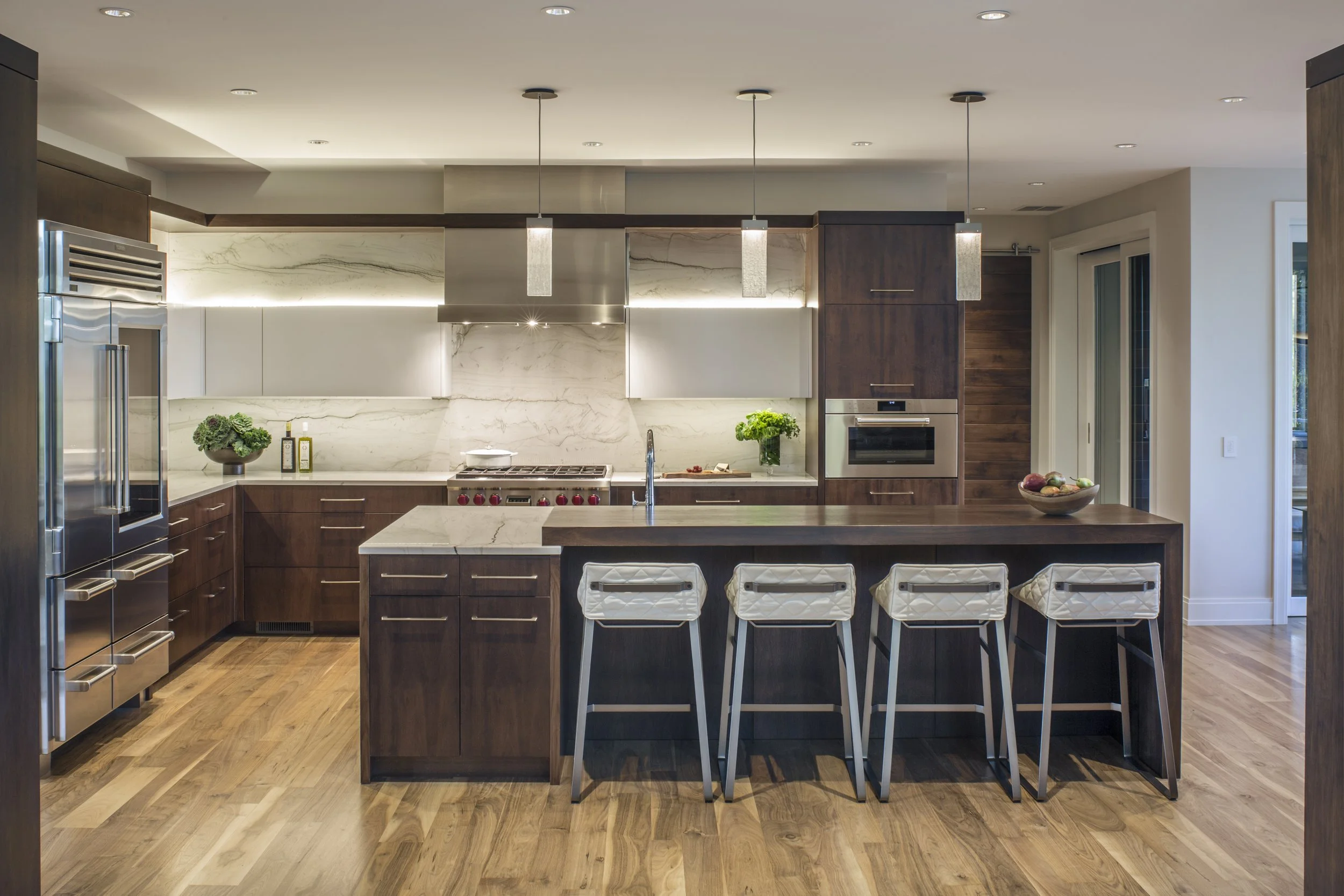 Modern kitchen with dark wood cabinets, white marble backsplash, stainless steel appliances, center island with seating, and hardwood flooring.