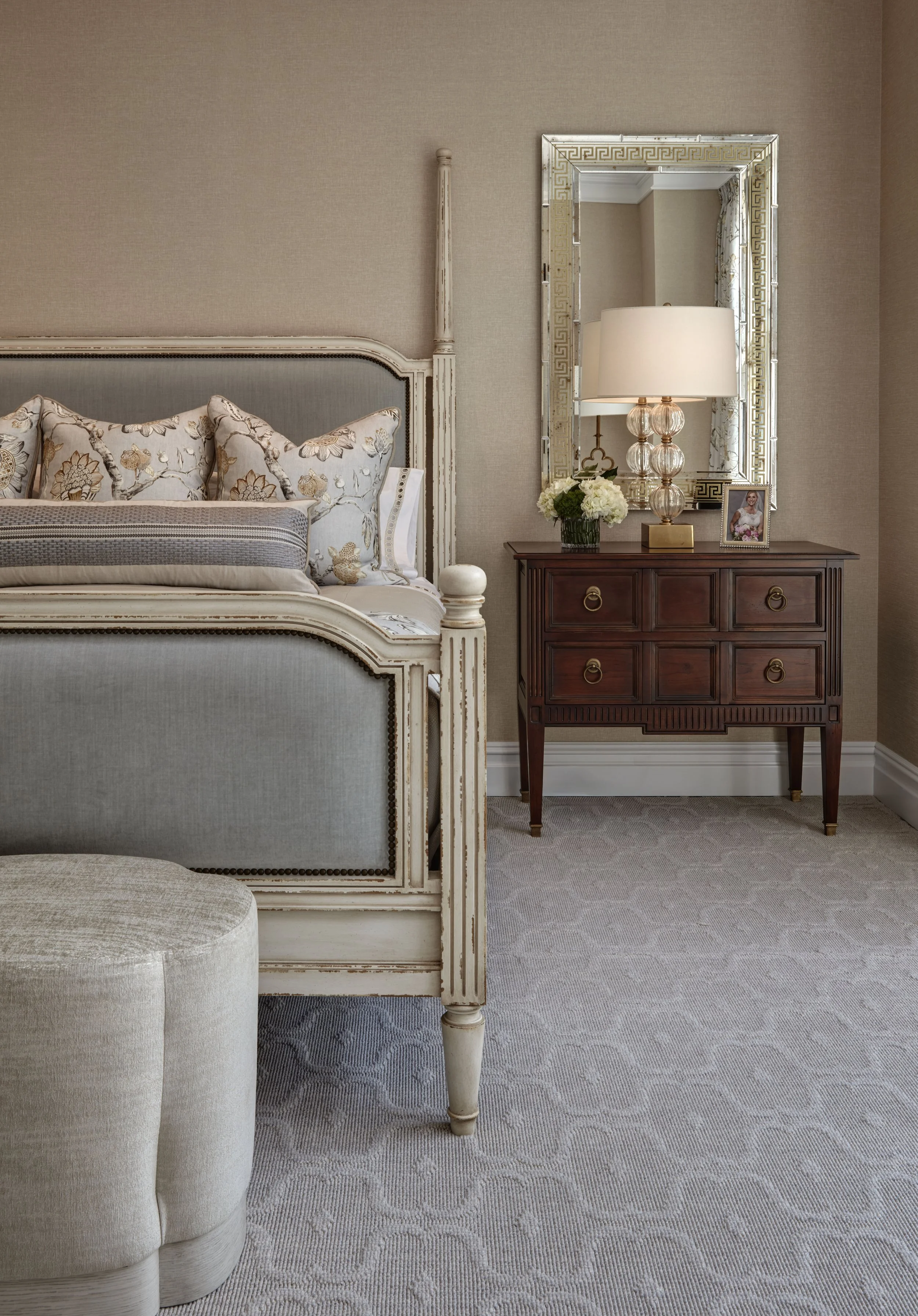 A bedroom corner with a decorated bed, wooden nightstand, and mirror.