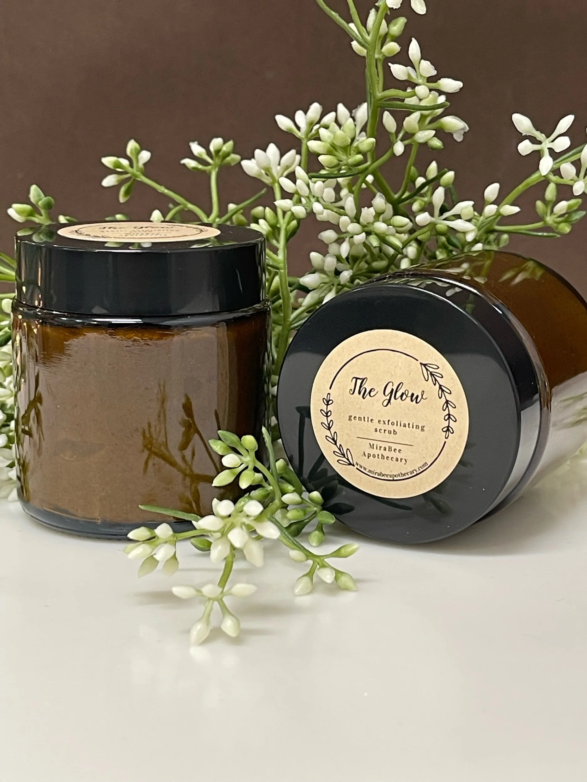 Jars of exfoliating scrub with white flowers.