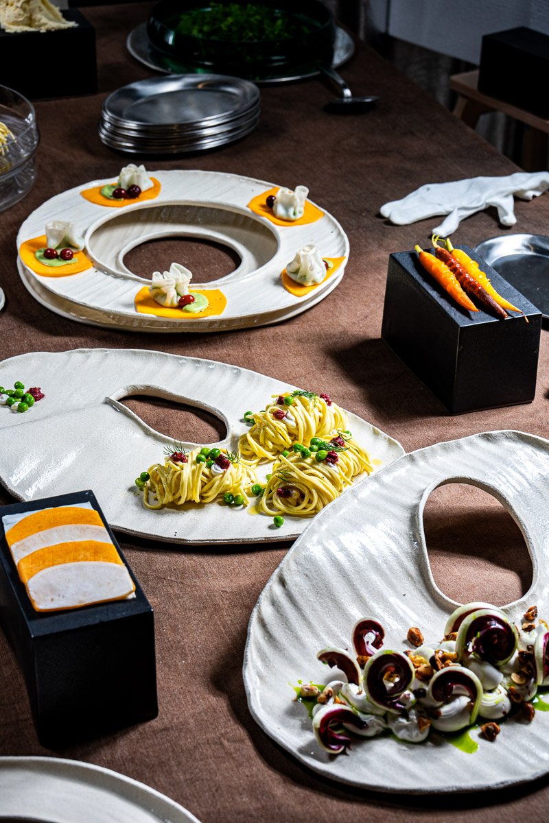 A table with decorative plates holding appetizers and garnished salads, surrounded by utensils and serving dishes in a dining setting.
