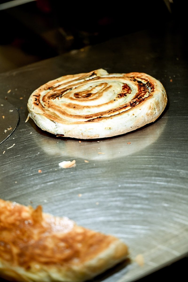 A cinnamon roll on a baking sheet with some crust in the foreground.