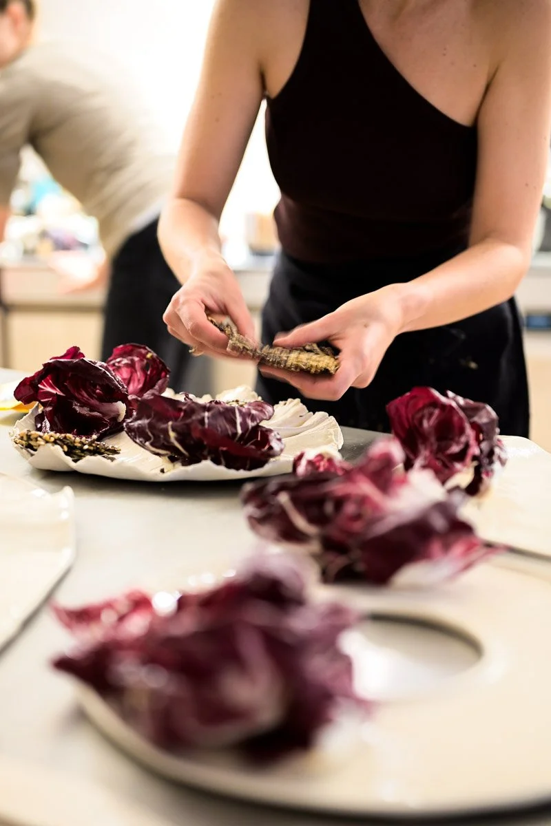 A person is preparing radicchio leaves on a kitchen counter, with a plate of radicchio and other ingredients in the background.