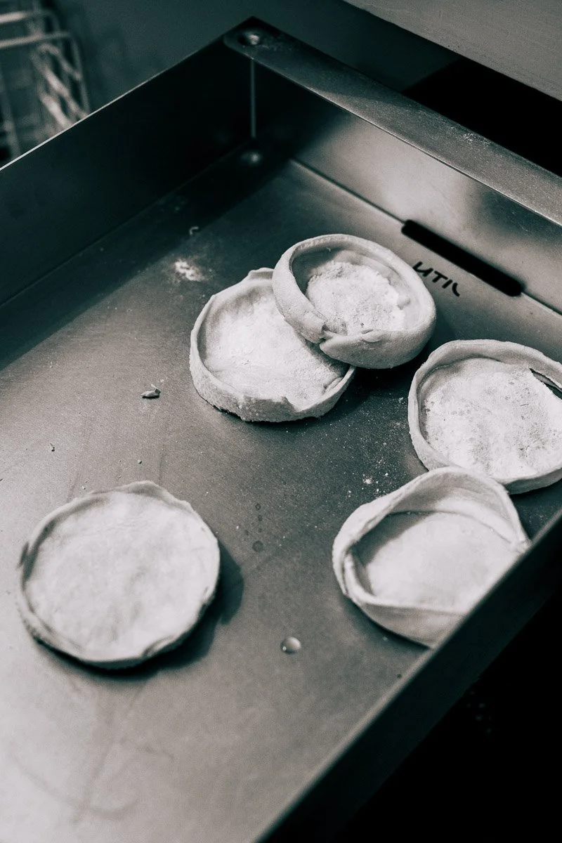 Six empty pastry shells on a metal baking sheet, dusted with flour.