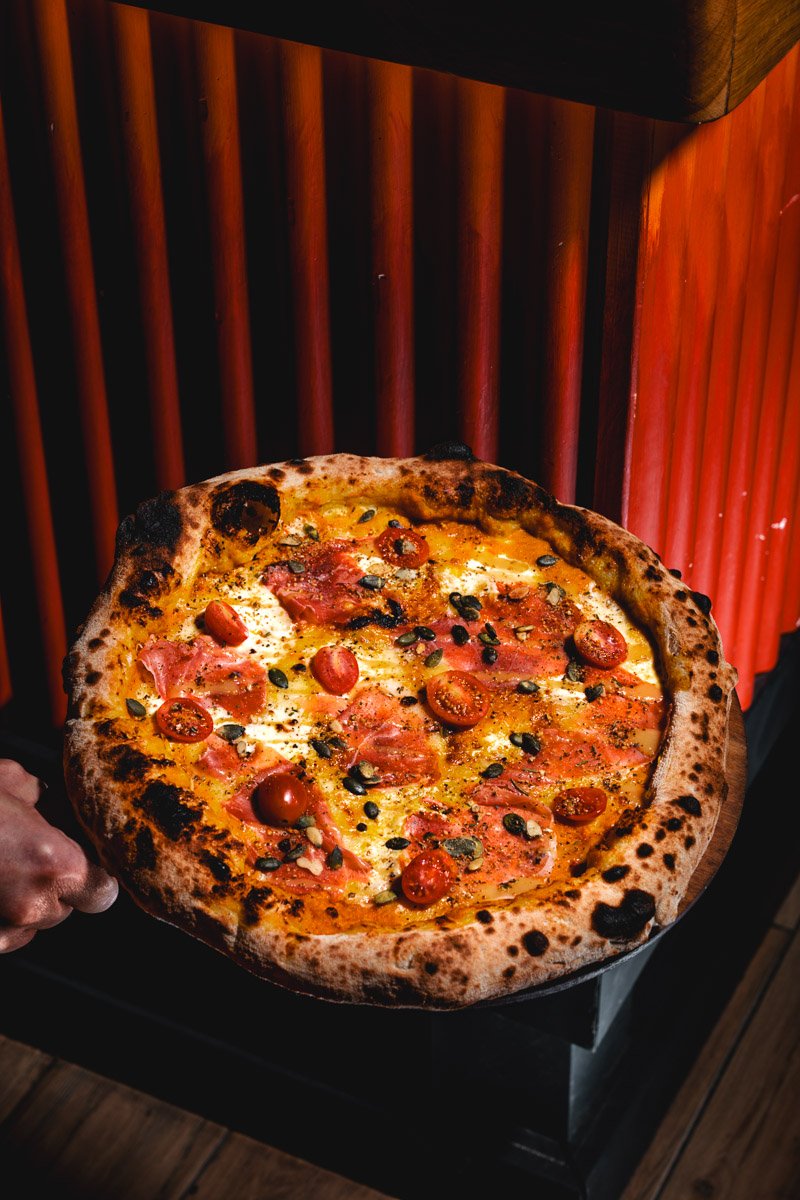 A freshly baked pizza with cherry tomatoes, black olives, sliced ham, and melted cheese on a baked crust.