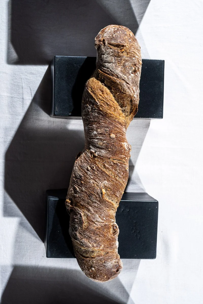 A large, elongated piece of root vegetable, possibly a yam or taro, placed on a black stand against a light background with shadows.