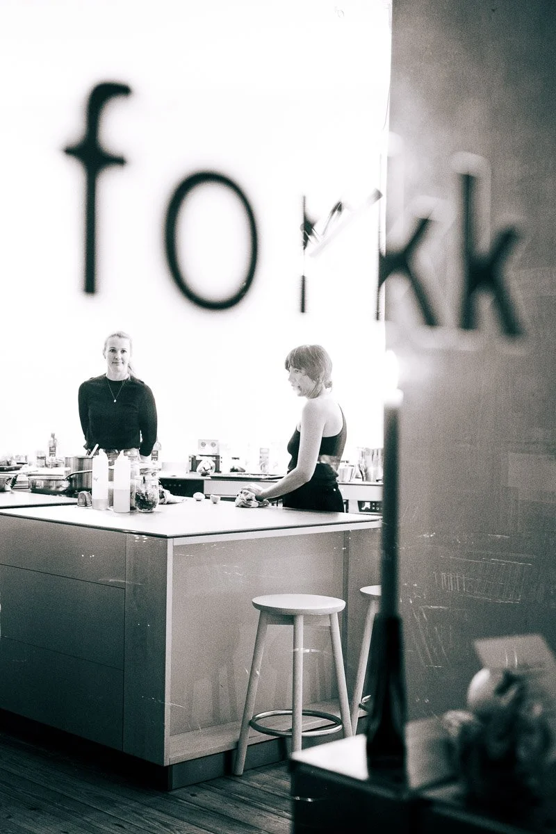 Two women preparing food in a modern kitchen, seen through a frosted glass with the word 'fork' partially visible.