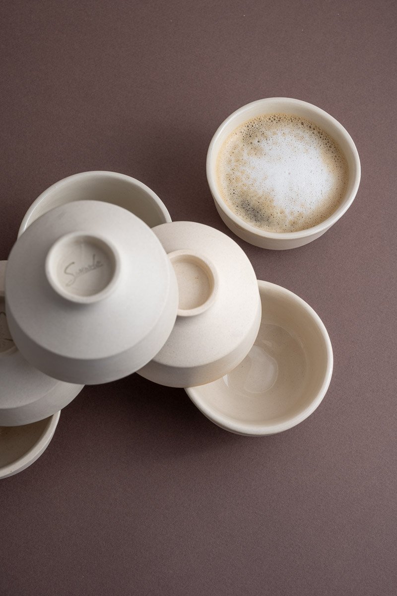 Several stacked white ceramic cups, one with foam on top, on a brown surface.