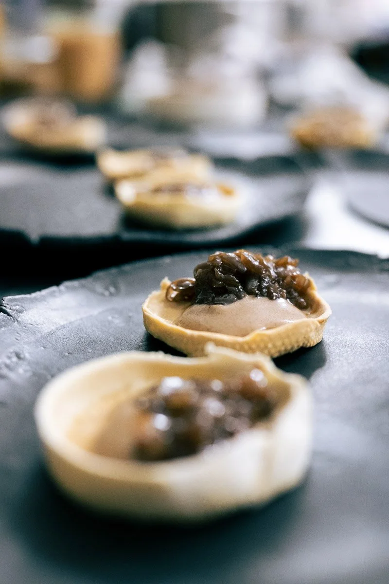 Close-up of two uncooked dumplings filled with a brown filling on a black surface, with more dumplings in the background.