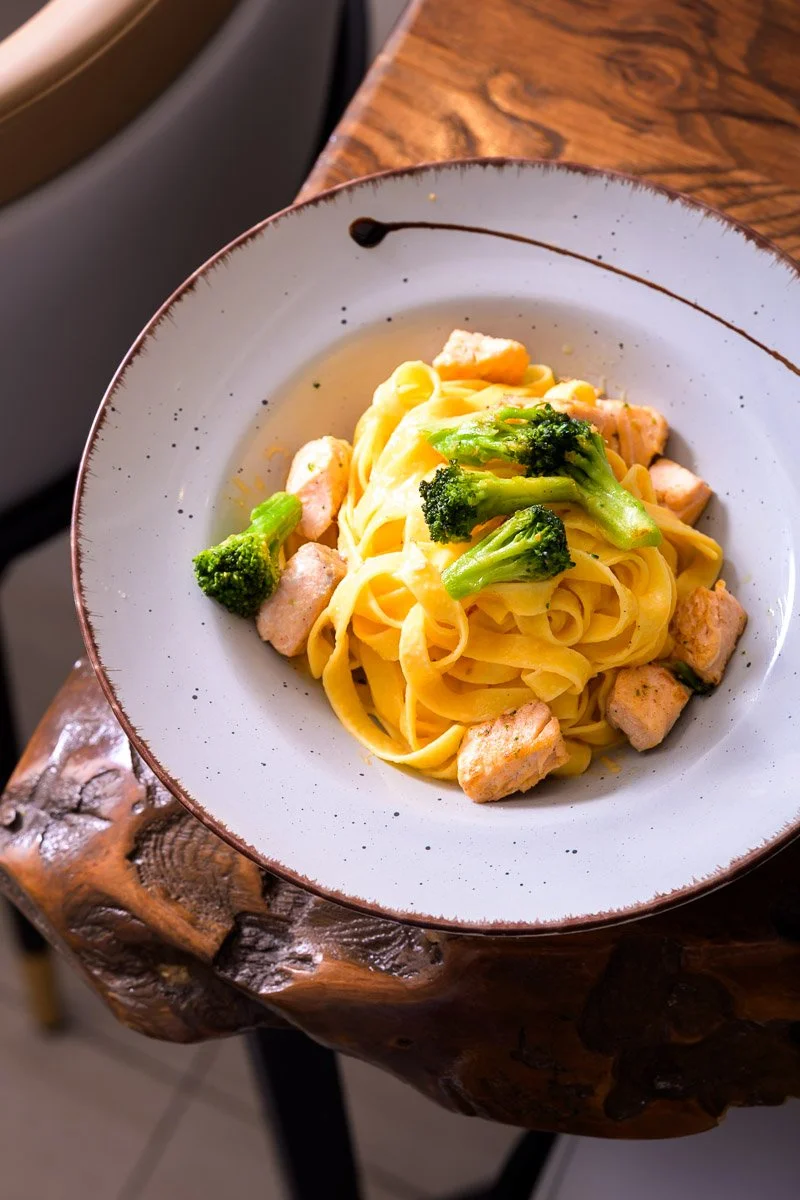 A plate of fettuccine pasta with broccoli and pieces of chicken on top, served on a rustic wooden table.