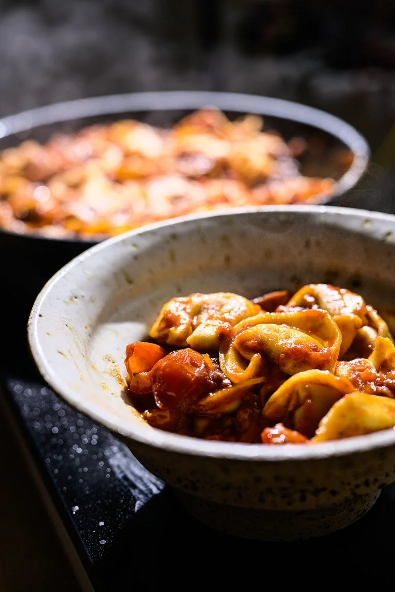 Close-up of a bowl of tortellini in tomato sauce, with another bowl of pasta in the background.