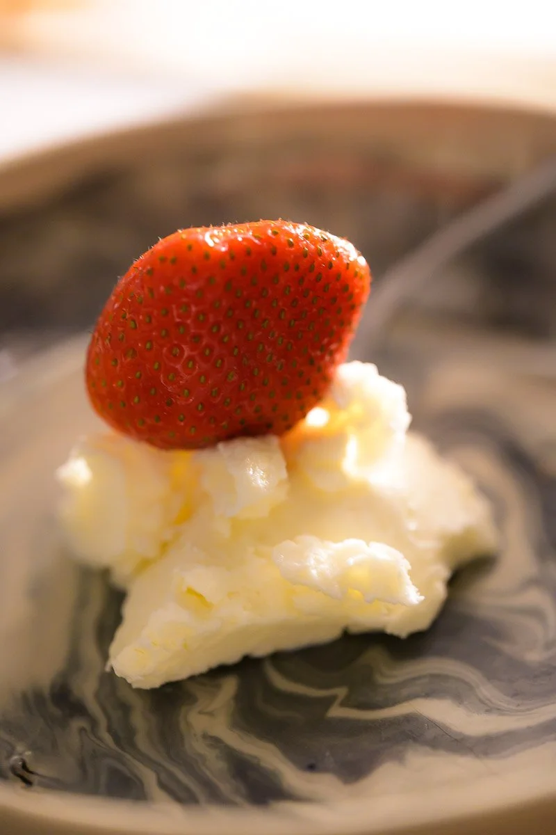 Strawberry on top of a dollop of whipped cream or yogurt on a patterned plate.