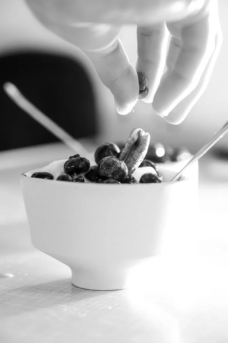 Hand sprinkling blueberries and other berries into a bowl.