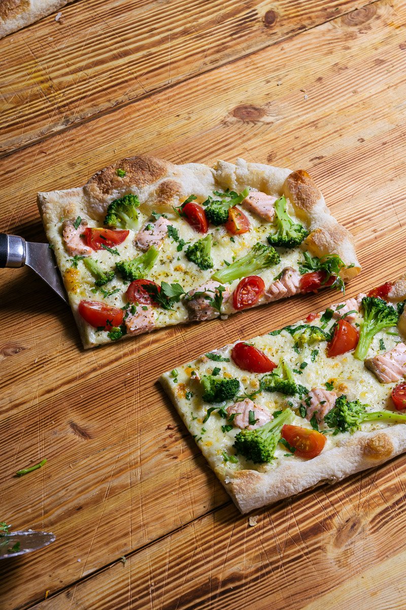 Two slices of pizza with broccoli, cherry tomatoes, chicken, and melted cheese on a wooden surface.